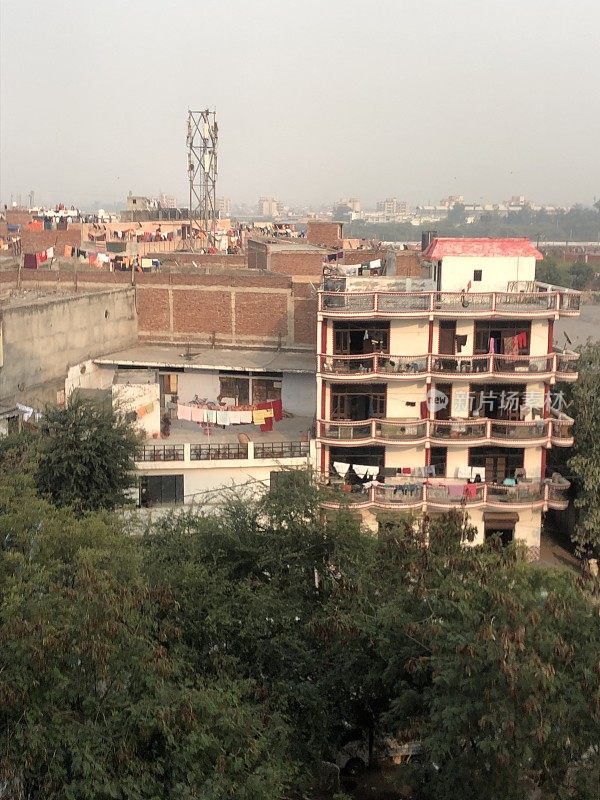 这是印度新德里的公寓楼屋顶，晾衣线上挂满了衣服，展示了早晨朦胧的天空污染的景象，被污染的雾蒙蒙的天空，汽车尾气/工厂排放的污染照片